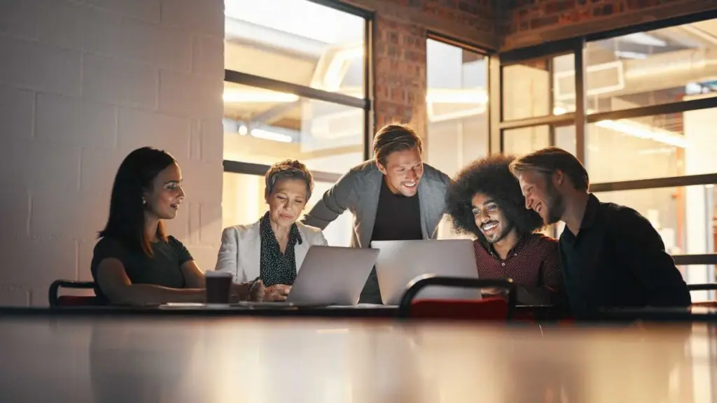 "Enthusiastic team collaborating around a laptop in a modern office environment, emphasizing teamwork, coworking, and project development in creative workspaces."