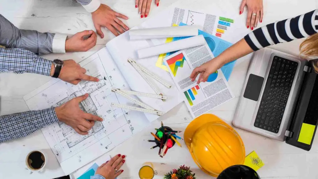 "Project planning session with multi-disciplinary team reviewing architectural blueprints and colorful charts, highlighting construction project management and teamwork."