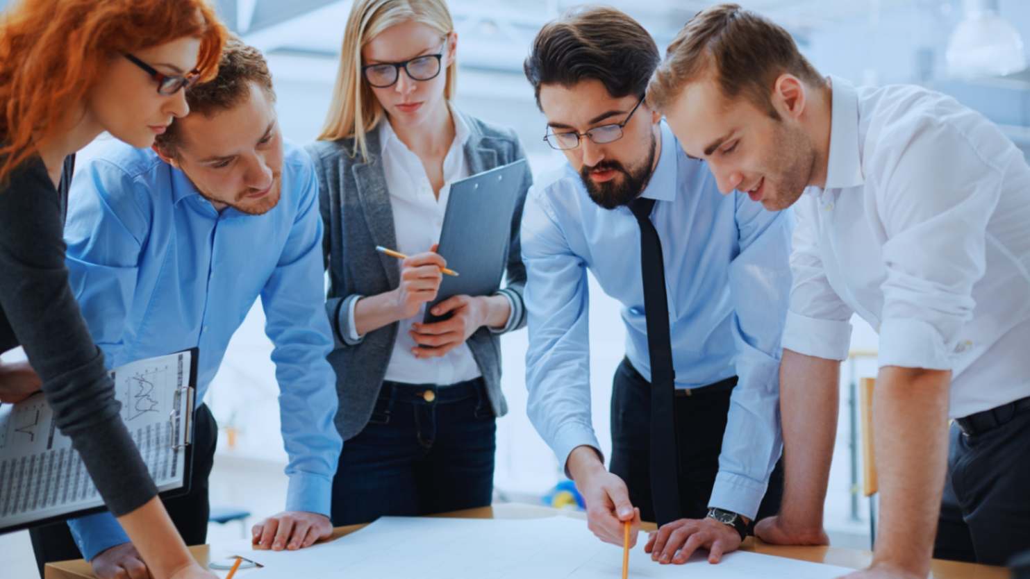 Group of business professionals discussing project plans over architectural drawings in a modern office environment.