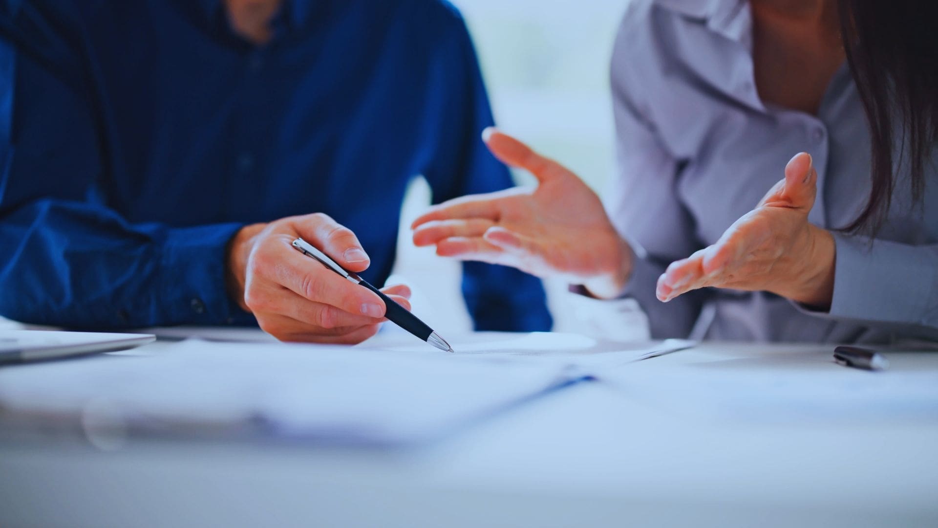 Two business professionals discussing documents, focusing on strategic planning in a blue-toned office.