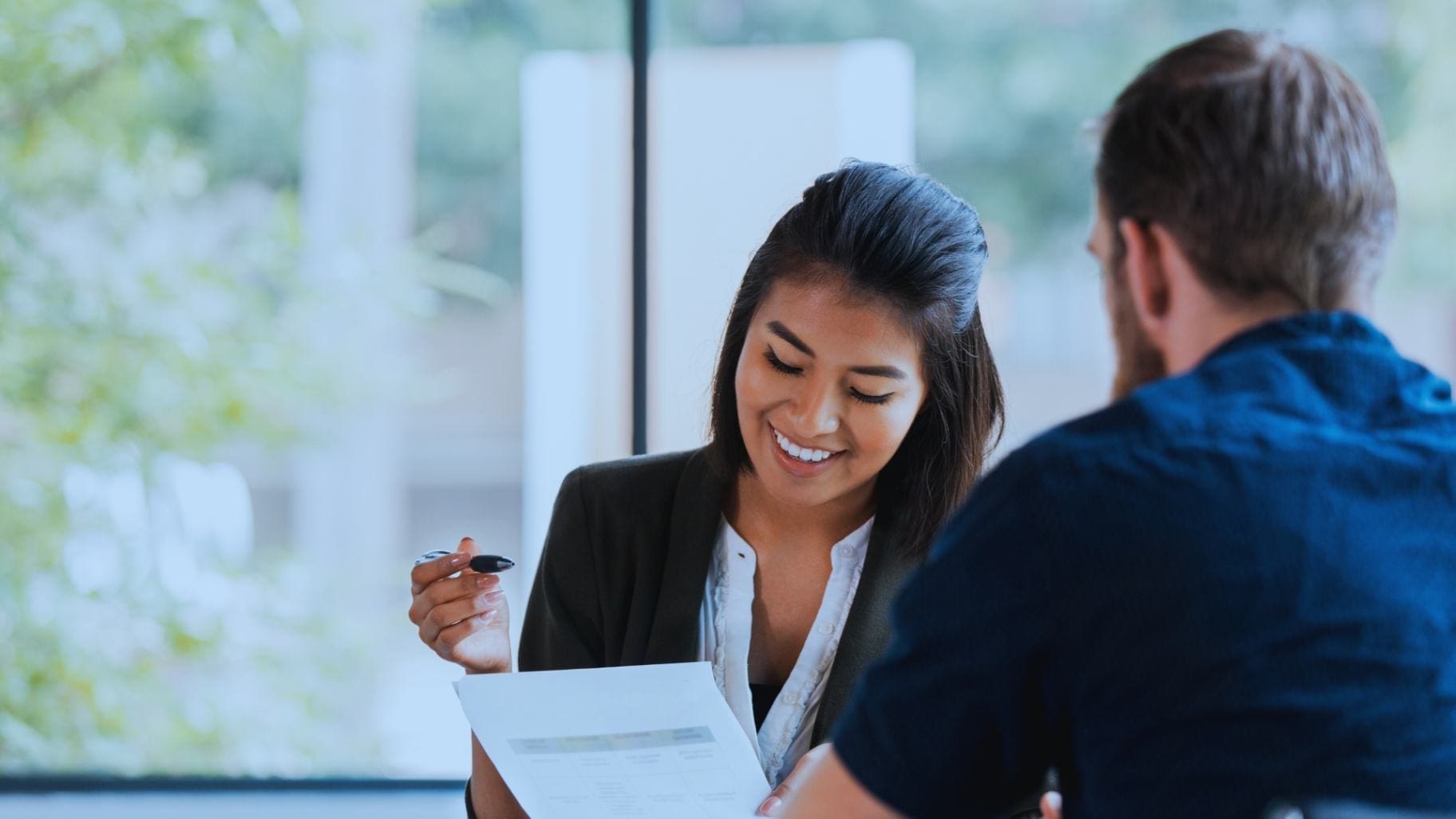 Businesswoman smiling while discussing a document with a colleague in a bright office.