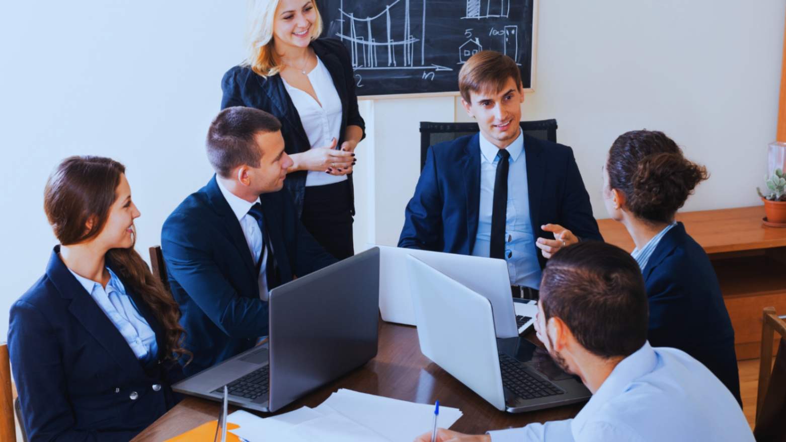 Business team meeting in a conference room, discussing strategies with laptops and digital devices.