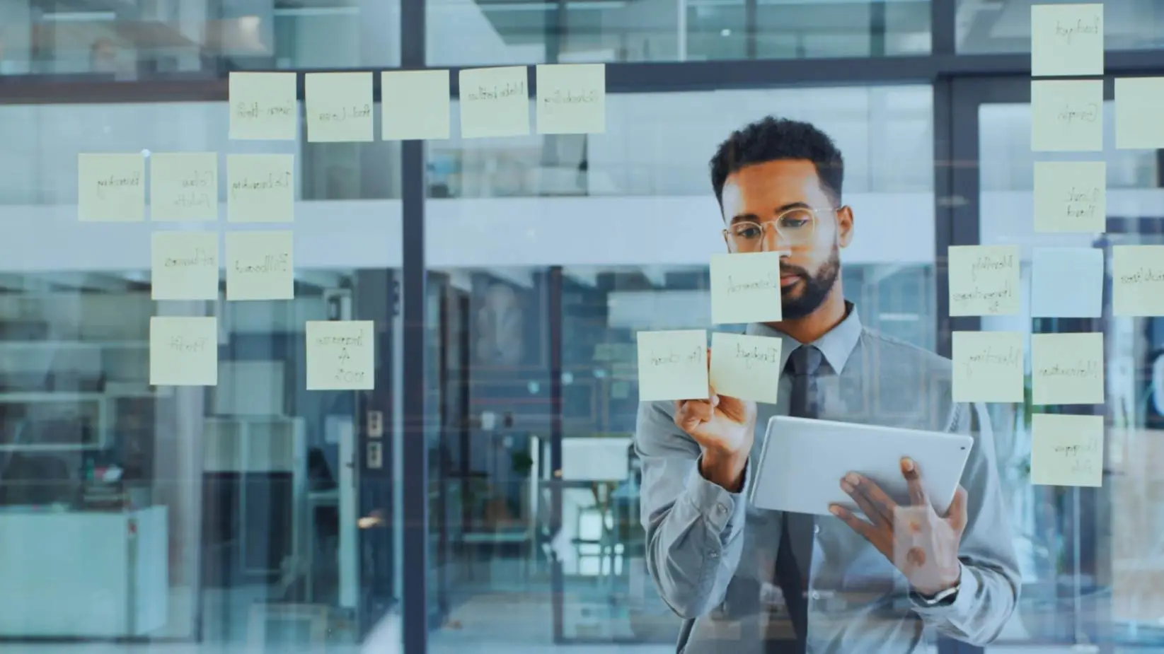 "African American businessman analyzing a strategic planning session using sticky notes on a glass wall in a bright office environment."