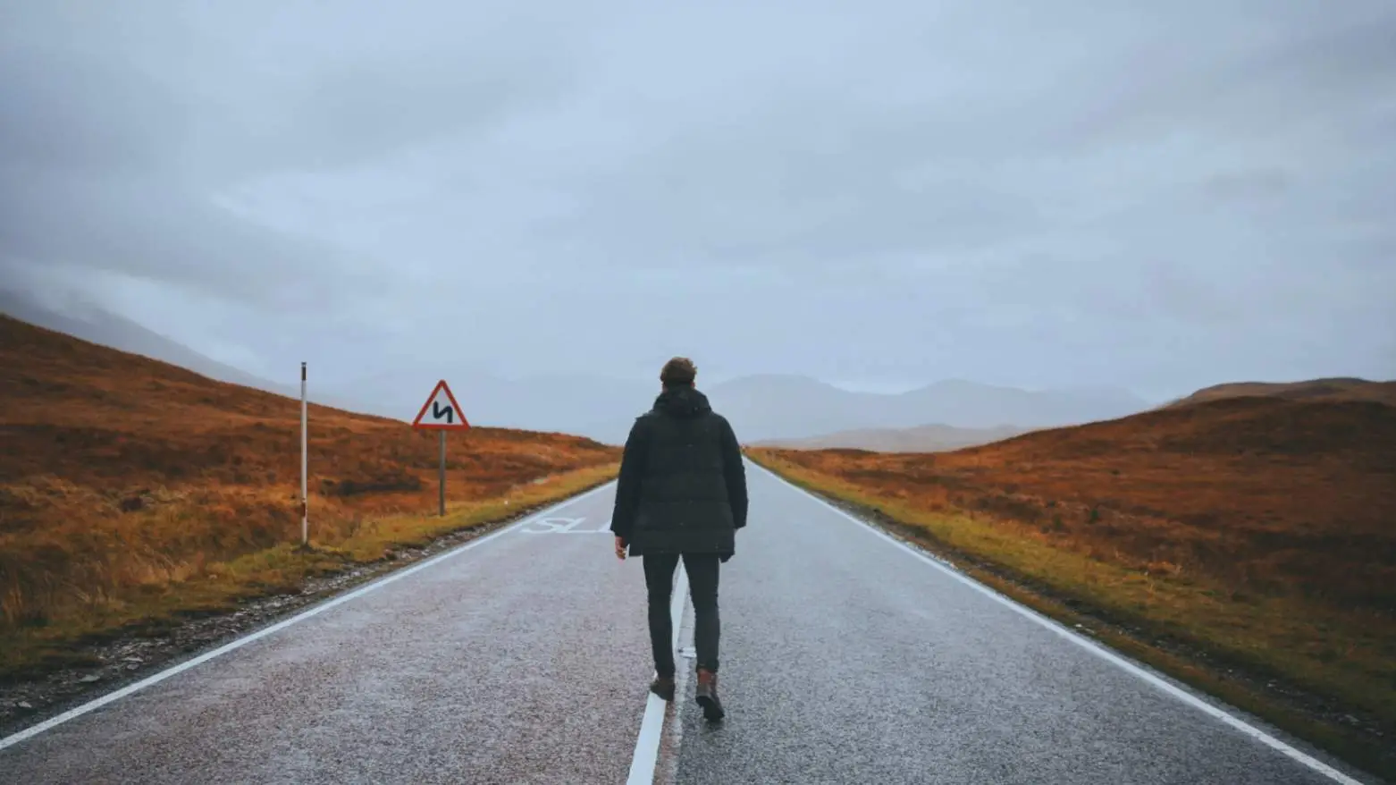 "Lone man walking on a deserted road in a scenic mountainous area, symbolizing challenge, journey, and solitude."