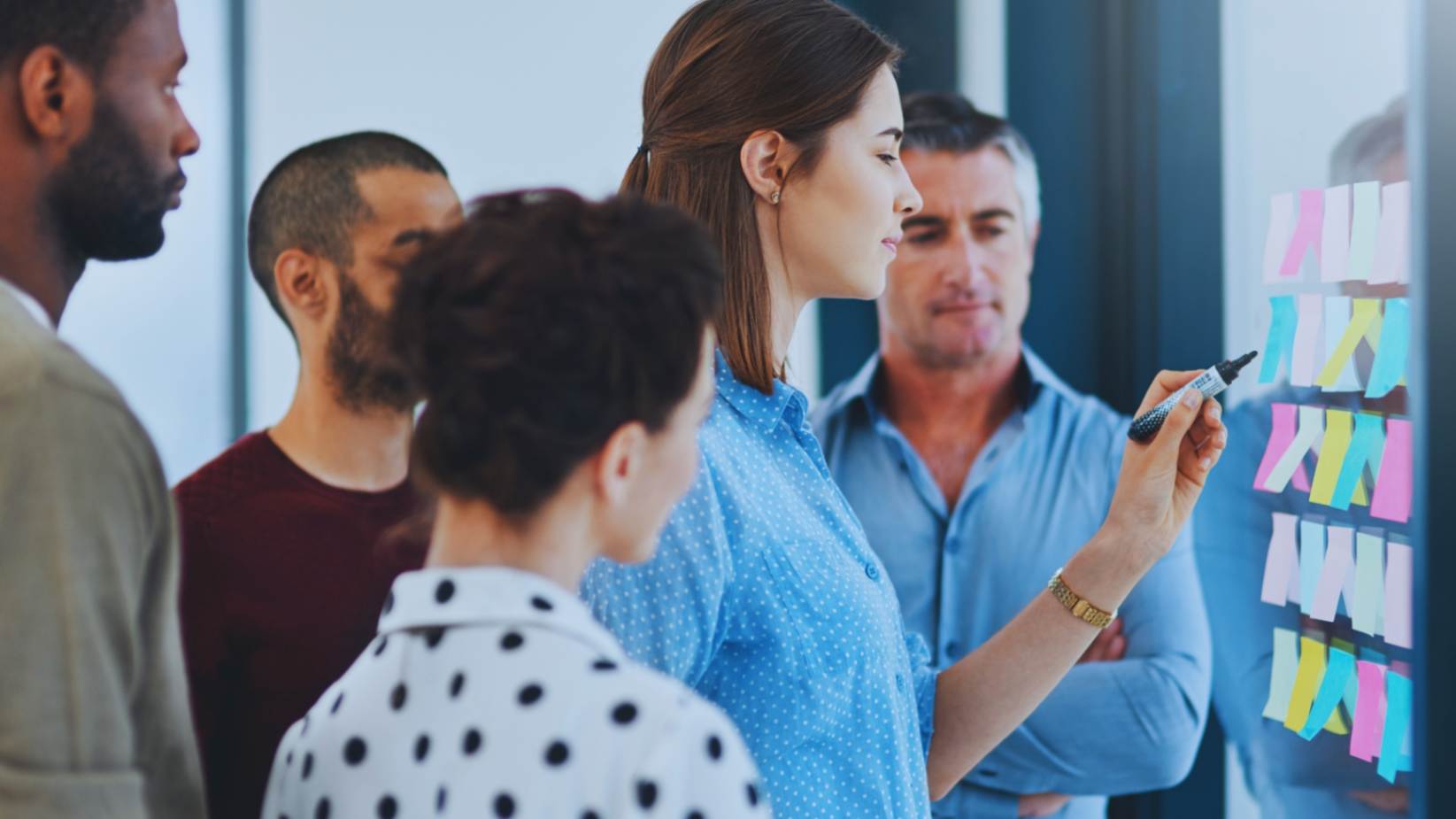 Diverse team of professionals engaging in a strategic workshop with colorful sticky notes in a modern office.